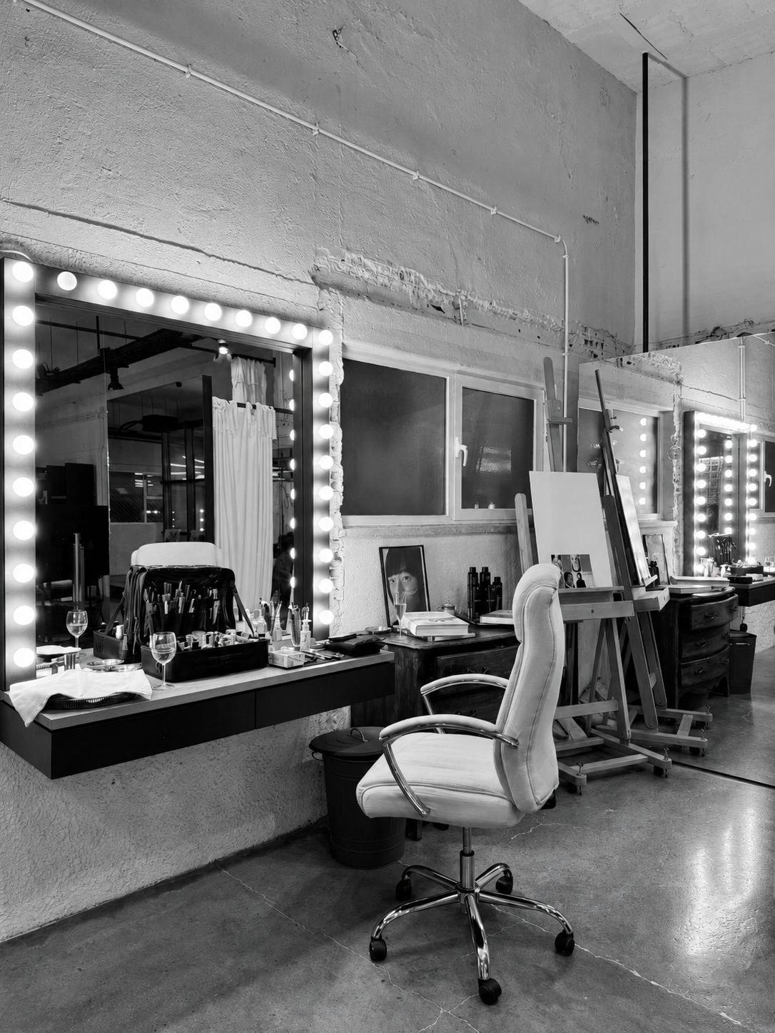 Black and white photograph of a studio dressing room with illuminated vanity mirrors and a white chair